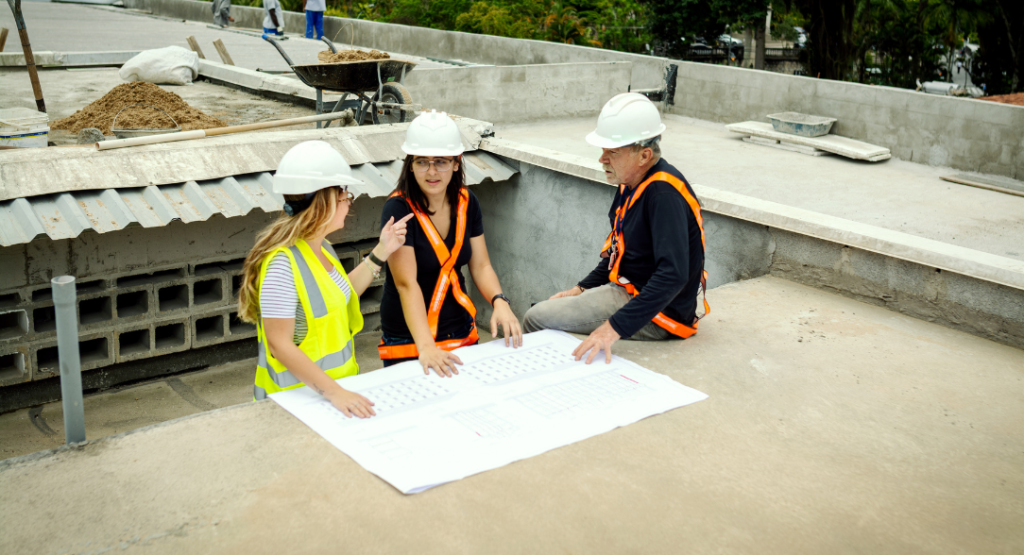 Equipe de engenharia analisa projetos no canteiro de obras para identificar e corrigir não conformidades na construção.