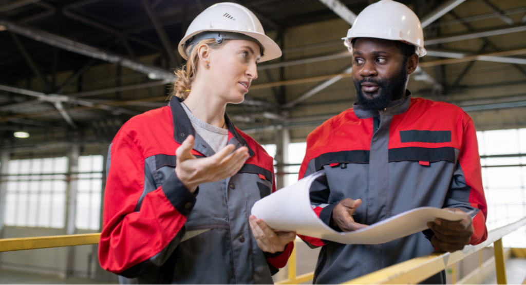 Dois profissionais de engenharia discutindo detalhes técnicos com plantas em mãos, focados no planejamento de obras eficiente.